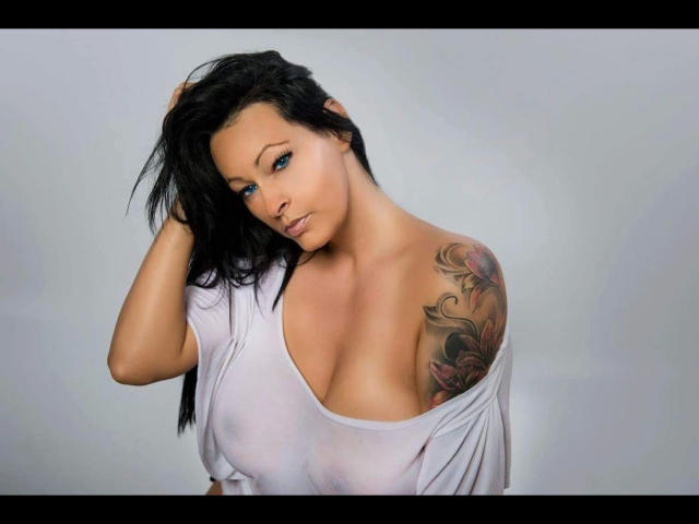 TaliaVaiolet-hot with black hair, blue eyes, and a tattoo on her right shoulder, wearing a white, wet, see-through shirt, showing her big, bare tits.