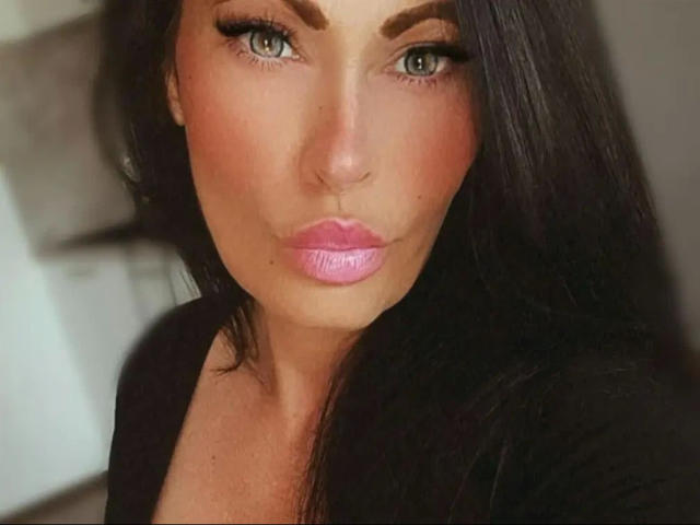 TaliaVaiolet-hot has pouty pink lips, full tits, and dark, wavy hair, with a serious expression and subtle makeup, green eyes, and a slightly tanned, smooth face.