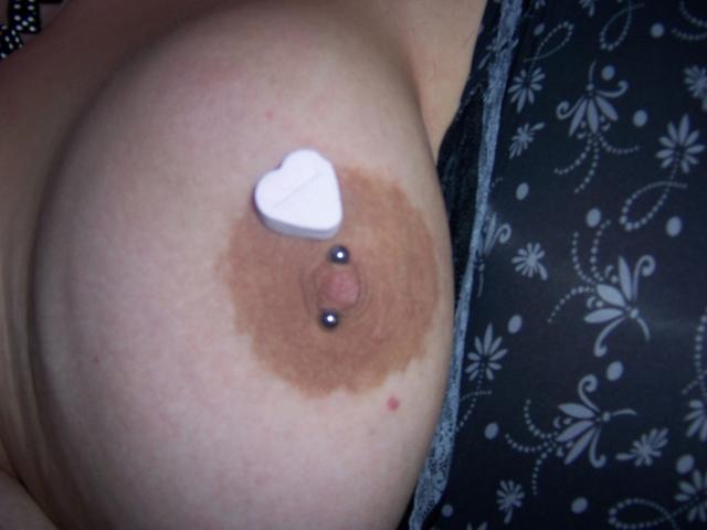 Scharfe-kitty's tits, showing a brown areola with a nipple piercing and a white heart-shaped pastie. Her skin is light and the photo is a close-up.