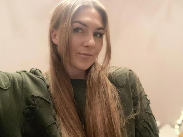 GanzNettePaola-hot with long, wet brown hair, green eyes, and a subtle smile, wearing a green, textured jacket, looking to the side. Her tits are small, and she's cute.