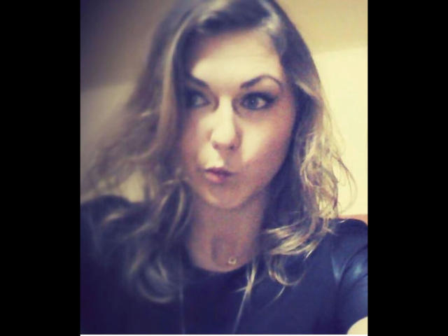 GanzNettePaola-hot with blonde wavy hair, pouty lips, and dark eyeliner, wearing a black shirt, in a blurry selfie. Her tits are slightly visible, and she's giving a pout.
