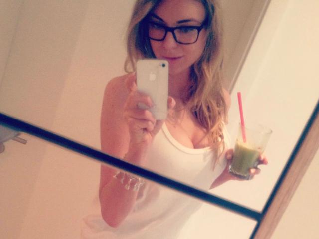 SativaExlusive-hot with glasses, blonde hair, white tank top showing her tits, holding a drink with a red straw in a mirror selfie. Her iPhone is in her right hand.