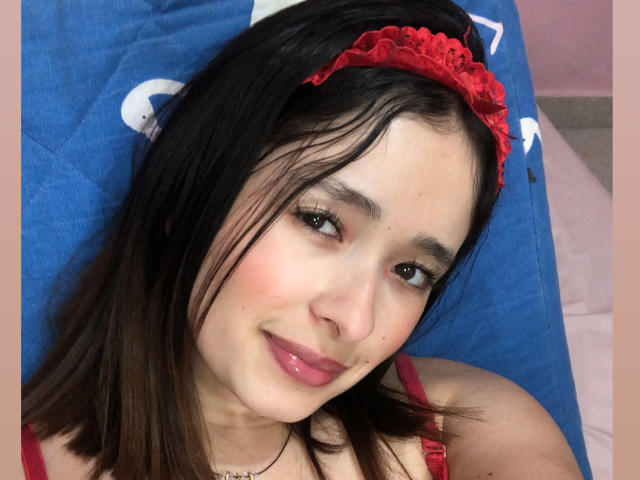 ElinaLeducc has straight brown hair, a red lace headband, and a slight smile with pink lipstick, showing her cute face and small nose. She's wearing a red top.