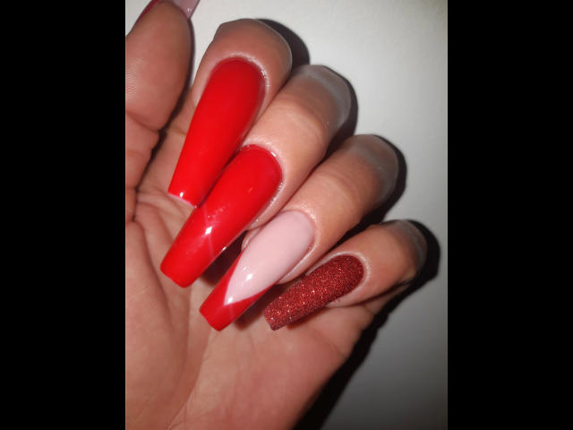 Kostlich-hot's hand with super long, shiny red and pink nails, plus one glittery red nail, against a dark background. Boobs-sized nails are sexy.