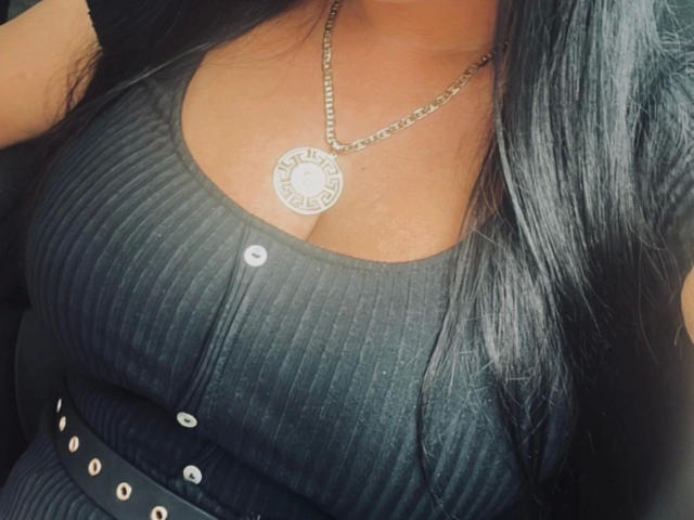 Larisssa21-hot's black ribbed shirt with buttons, showing her large boobs, and a silver chain with a circular pendant. Her long black hair is on the right.
