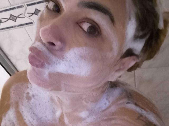 SolmaryHot with soapy foam covering her nose, lips, and upper chest, looking up with brown eyes and slightly raised eyebrows, in a bathroom. Her tits are partly visible.