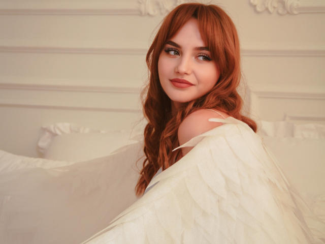 Camilla Roberts, avec des cheveux roux, des ailes blanches, souriante, regardant par-dessus son épaule, montrant son épaule nue et le haut de son dos, lumière douce, expression douce..