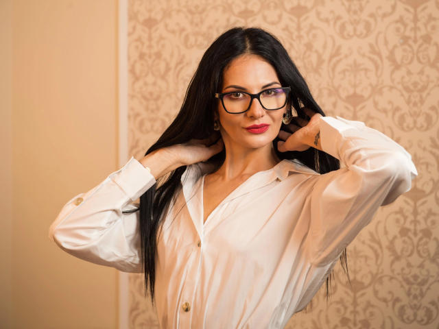 SinaRauch-hot with long black hair, glasses, red lipstick, white button-up shirt, hands in hair, smiling, looking at camera, subtle makeup, cute, attractive.