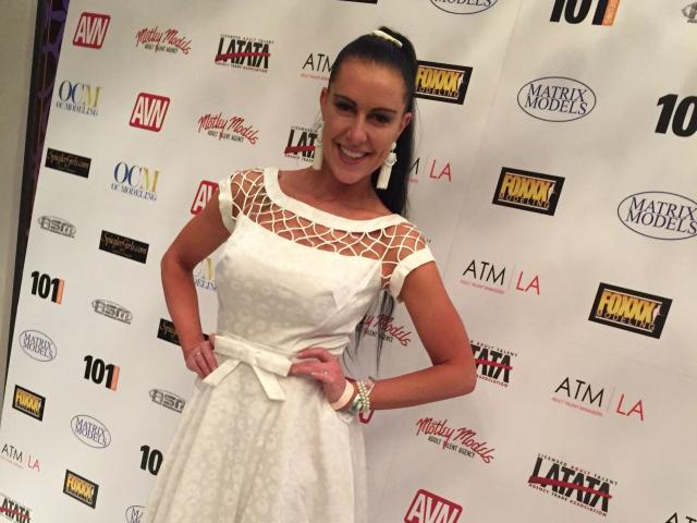 Texaspatti-hot with tan skin, dark brown hair in a ponytail, white dress with lattice top, smiling, hands on hips, wearing white earrings and bracelet, standing in front.