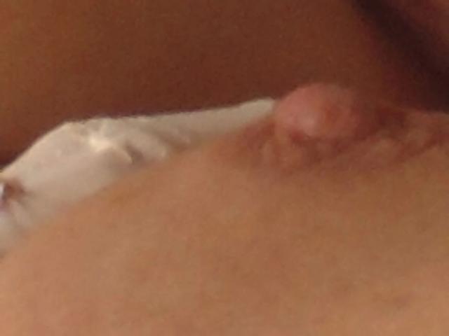 Reallive1-hot's small, pink nipple is in the center of the image, slightly raised and textured, with a blurred, warm-toned background.