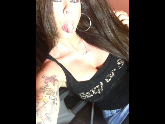 Cindy: ragazza attraente con lunghi capelli castani, che mostra la lingua, indossa una canotta nera con scritte dorate, ha un seno abbondante, un tatuaggio sul braccio destro, orecchini a cerchio e jeans blu..