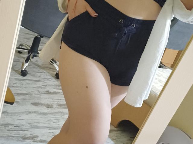 Leiliia's black booty shorts with lace-up front, white shirt open, showing her bare, pale, slightly curved, and smooth lower torso and thigh with a small mole.