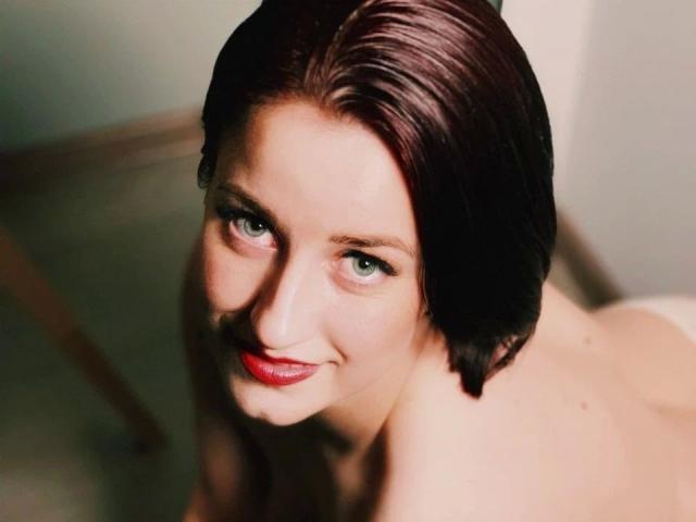 ChristineLove-hot with short brown hair, green eyes, and red lipstick, smiling at the camera, topless, showing her bare shoulders and a hint of her boobs.
