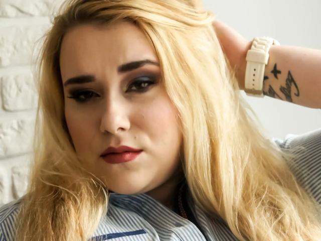 HaileyBLONDE-hot with blonde hair, dark eye makeup, red lipstick, hand in hair, white watch, tattoo on wrist, wearing striped shirt, looking slightly annoyed.