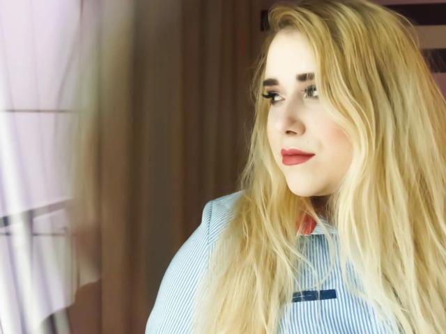 HaileyBLONDE-hot with blonde hair, blue eyes, red lipstick, and striped shirt, looking to the side with a slight smile. Her tits are not visible.