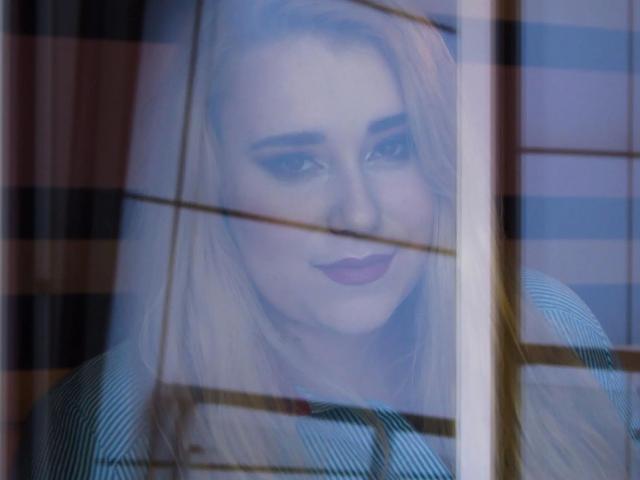 HaileyBLONDE-hot with pouty lips, blonde hair, and subtle makeup, looking through glass with striped patterns, her tits slightly visible, wearing a striped top, blue eyes, soft smile.