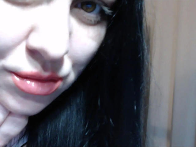 yourErica-hot's pale face with black hair, brown eyes, and shiny red lips, slightly upturned nose, hand gently touching her chin, soft blue lighting, close-up shot.