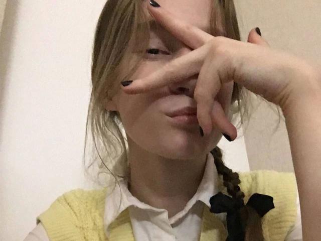 Enigma-hot with blonde hair in a braid, covering eyes with right hand, black nail polish, yellow cardigan, white shirt, black ribbon, pouty expression, light skin, medium build.