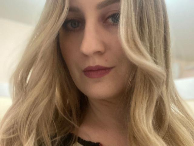 Kristinakokietka-hot with long blonde wavy hair, light skin, and red lipstick, staring at the camera with a subtle smile, wearing a black top, showing her cute face.