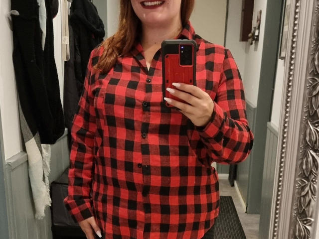 SiegruneValkyra - vestindo uma camisa xadrez vermelha e preta, segurando o celular no espelho, unhas vermelhas, sorrindo, mostrando os seios, cabelo castanho, em pé dentro de um armário, com a mão na cintura..