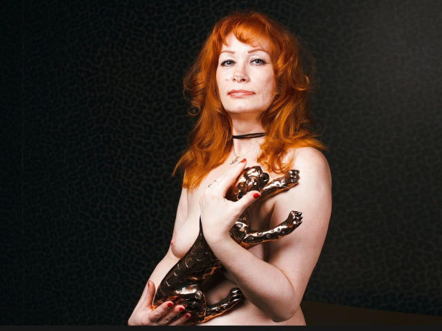 MomAimy-hot with red hair, holding a bronze statue of a leaping deer, covering her bare tits with her hands, wearing a black choker, looking confident.