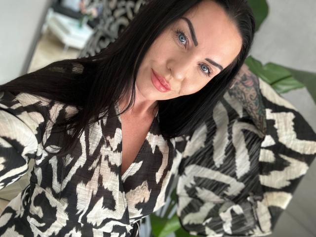 Malina-Lay met lang zwart haar, blauwe ogen en roze lippen, draagt een zwart-wit gestreept top, toont haar getatoeëerde arm, maakt een selfie en glimlacht lichtjes..
