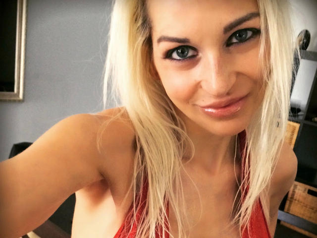 Jackylafey-hot with blonde hair, green eyes, and shiny lips, wearing a red halter top, smiling at the camera, showing her tits. Her ass is not visible.