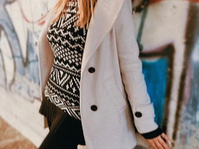 Victoria-Diamond with a white coat, black and white patterned top, black pants, and black buttons. Her ass is partially visible, and her blonde hair is down.