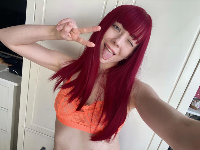 Jessie: Zeer aantrekkelijk met rood haar, knippend met haar oog, haar tong uitsteken, een vrede-teken maken, een oranje kantbeha dragen, bleke huid, kleine borsten, in een lichte kamer, selfie..