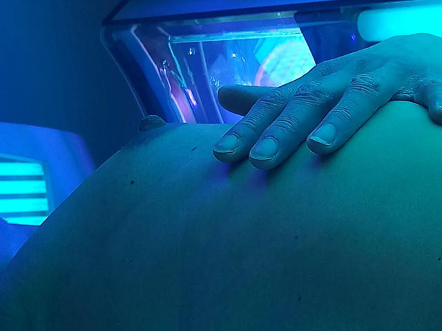 Sandyx-hot's hand rests on their bare ass under blue lighting, showing a close-up of their butt with a finger gently touching the skin.