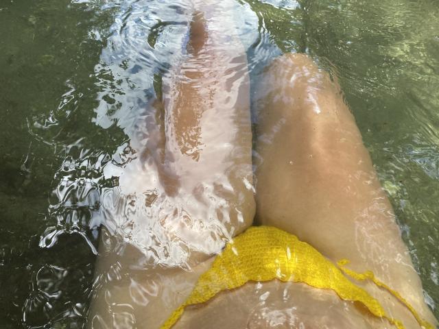 JuliaGarciax's legs in green water with a yellow crochet bikini bottom, her thighs and lower belly visible, her skin light and slightly reflective.