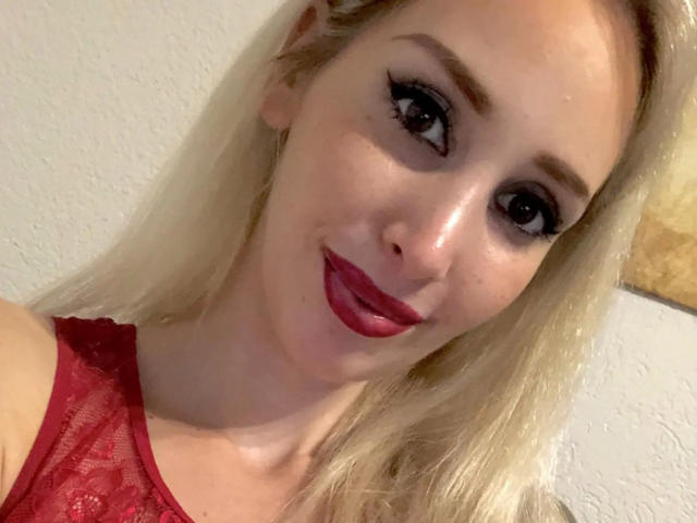 StellaCinderella-hot with blonde hair, red lace top, and dark red lipstick, smiling at the camera with slightly parted red lips, showing off her cute face and big eyes.