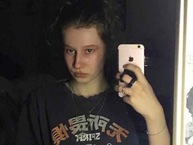 Enigma-hot with curly brown hair, pale skin, and pouty lips, wearing a dark shirt, holding an iPhone, looking into a mirror. Boobs not visible. Ass not visible. Pussy not visible.