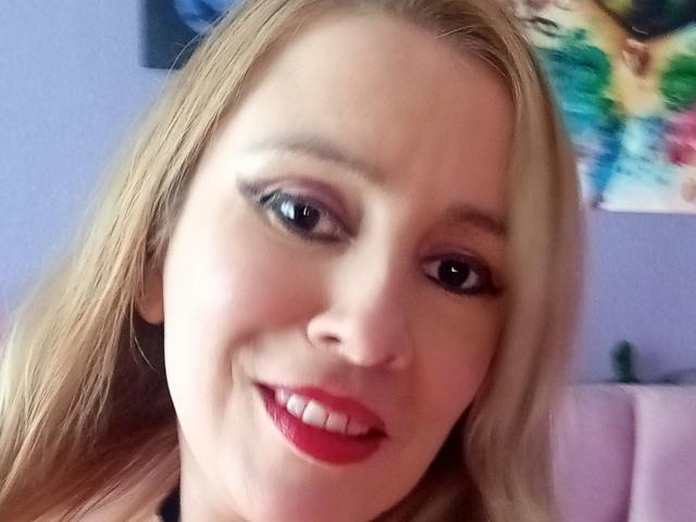 MadissonS a les cheveux blonds, les yeux bleus et porte du rouge à lèvres. Elle sourit, a un visage mignon et on voit ses dents. Ses fesses ne sont pas visibles sur l'image..