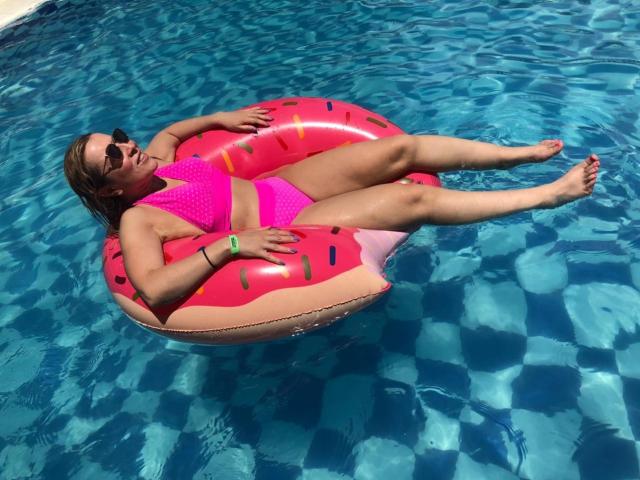 MadissonS está recostada en un flotador de sandía rosa, vistiendo un bikini rosa brillante, gafas de sol y una pulsera verde, flotando en una piscina azul cristalina. Sus pechos son pequeños y ella está relajada..
