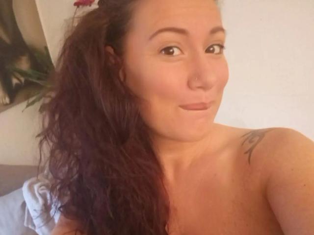 Vivien-Molinas hat welliges, braunes Haar, einen Nasenring und ein Tattoo an ihrer rechten Schulter. Sie ist oben ohne und trägt ein leichtes Lächeln, während sie in die Kamera schaut..