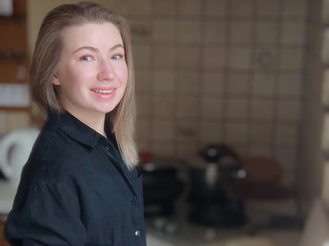 MiaFlirt with blonde hair, blue eyes, and a smile, wearing a black shirt, standing in a kitchen, showing a cute, sexy face with subtle makeup.