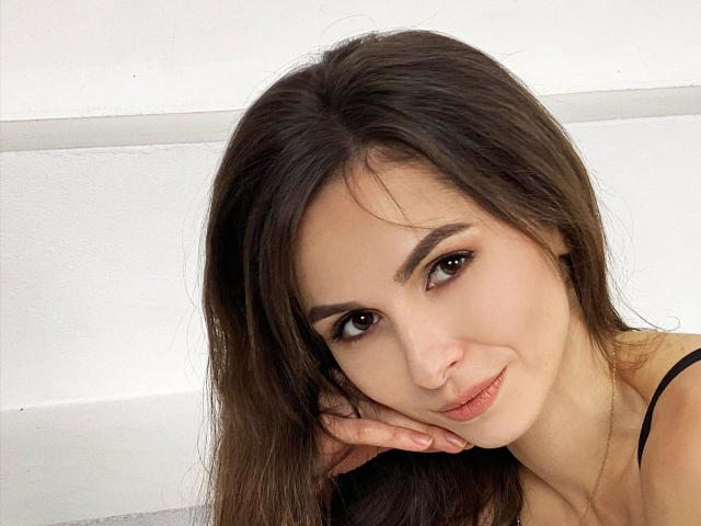 SweetPaulla-hot ha lunghi capelli castani, occhi castani e un sorriso carino. Ha la testa appoggiata sulla mano, mostrando la sua pelle morbida e un leggero lucidalabbra rosa..