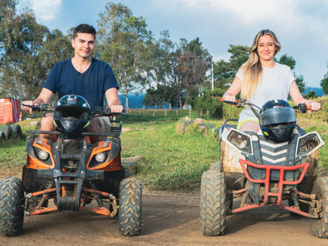 Angela e Max, com um traseiro atraente em uma moto de trilha, vestindo uma camisa branca, e Max com um traseiro flácido em uma moto de trilha laranja, ambos sorrindo ao ar livre..