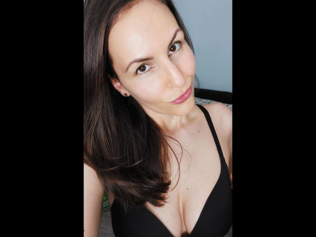 Schneewitchen1-hot with dark brown hair, wearing a black bra, showing cleavage, smiling slightly, and looking up at the camera.