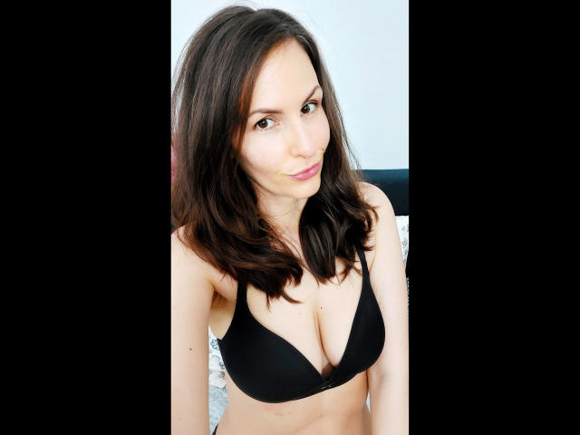 Schneewitchen1-hot with dark brown hair, wearing a black bra that shows her tits, smiling slightly, in a bedroom setting, looking at the camera.