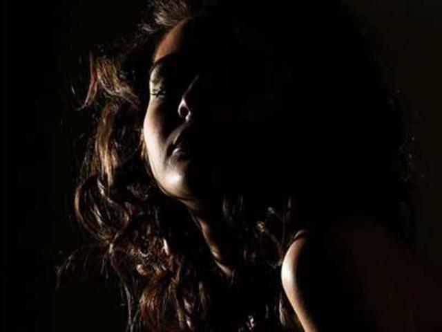 Darkly lit photo of Lovly19-hot with curly brown hair, green eyeshadow, and shadowed face, showing subtle boob outline in the dim light.