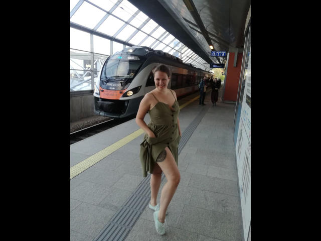 Suniabdsm-hot, con un trasero grande y pechos pequeños, vestida con un vestido verde y calcetines blancos, de pie en una plataforma de tren con un tren al fondo..