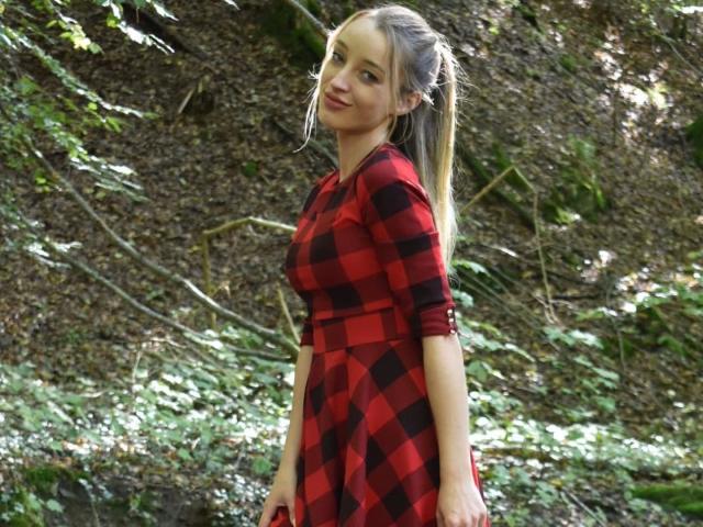CremeDeLaCremeDE-hot with long blonde ponytail, red-black checkered dress, small tits, slim, smiling, forest background, standing, hands by sides, sunlight filtering through leaves.