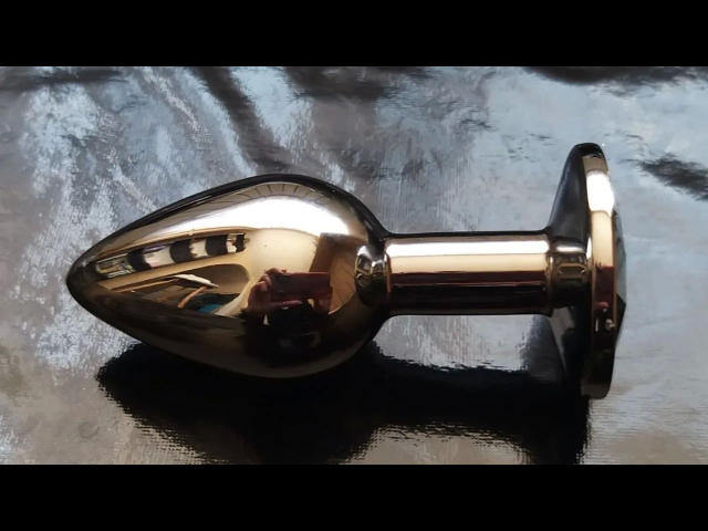 Glanzende, metalen plug voor de anus met een druppelvorm en een uitlopende punt, die licht reflecteert op een donker, glanzend oppervlak..