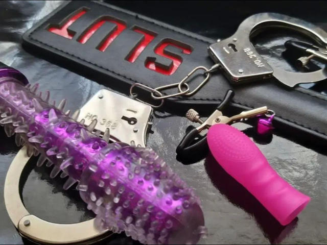 Paarse dildo met stekels, roze vibrator, metalen handboeien, zwarte leren riem en sleutelhanger van metaal op een glanzend zwart oppervlak. BDSM-speelgoed van Circea-hot..