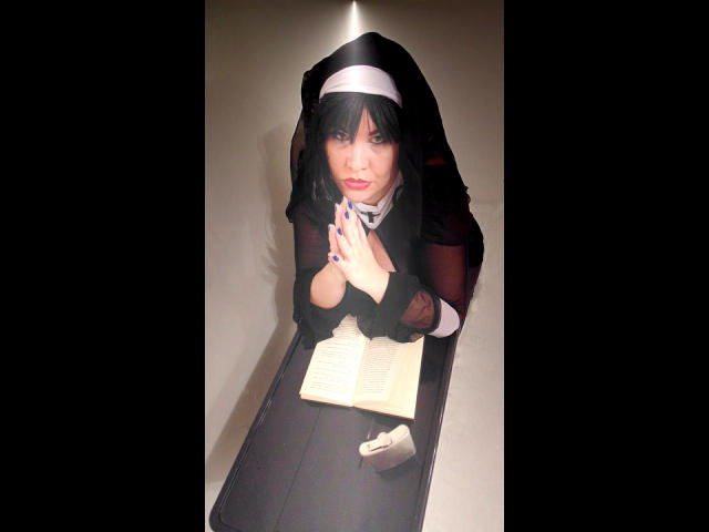 KatarinaArsch-hot with black hair, wearing a nun outfit, praying hands, black dress, white headpiece, black mesh sleeves, book on table, nails painted blue, serious expression, kneeling.