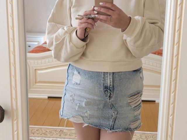 Goldmoon-hot with a white, fluffy sweater and a ripped, blue denim skirt, holding a phone in a mirror selfie, showing off her bare ass and white-painted nails.
