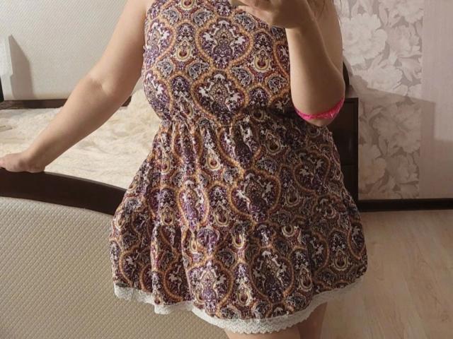 Goldmoon-hot wearing a purple and brown paisley dress with white lace trim, holding a mirror, showing her curvy tits and ass, pink bra visible on her right arm.