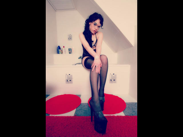 Wildandsexy25-hot with curly black hair, wearing black lingerie, sheer stockings, and black high heels, sitting on a white bathtub edge, legs crossed, looking seductively at the camera.